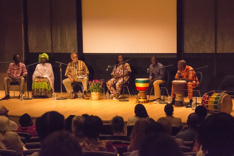 Panelists sit in a line facing the audience in chairs dressed in colorful garb